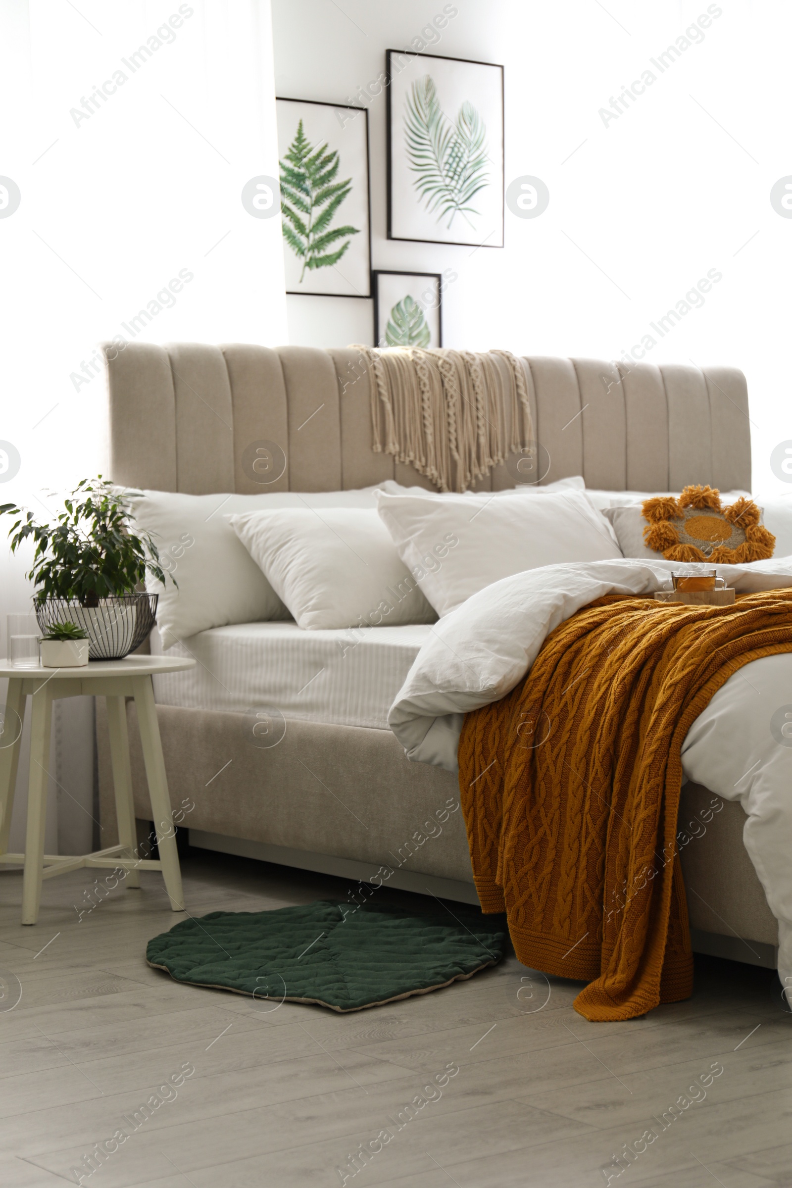 Photo of Comfortable bed with knitted orange plaid in stylish room interior