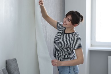 Photo of Woman hanging stylish gray wallpaper in room