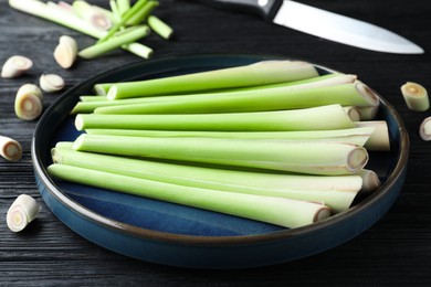 Photo of Plate with fresh lemongrass stalks on black wooden table, closeup