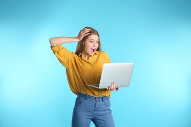 Emotional young woman with laptop celebrating victory on color background