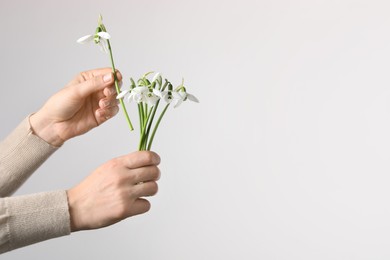 Woman holding beautiful bouquet of snowdrops on light background, closeup. Space for text