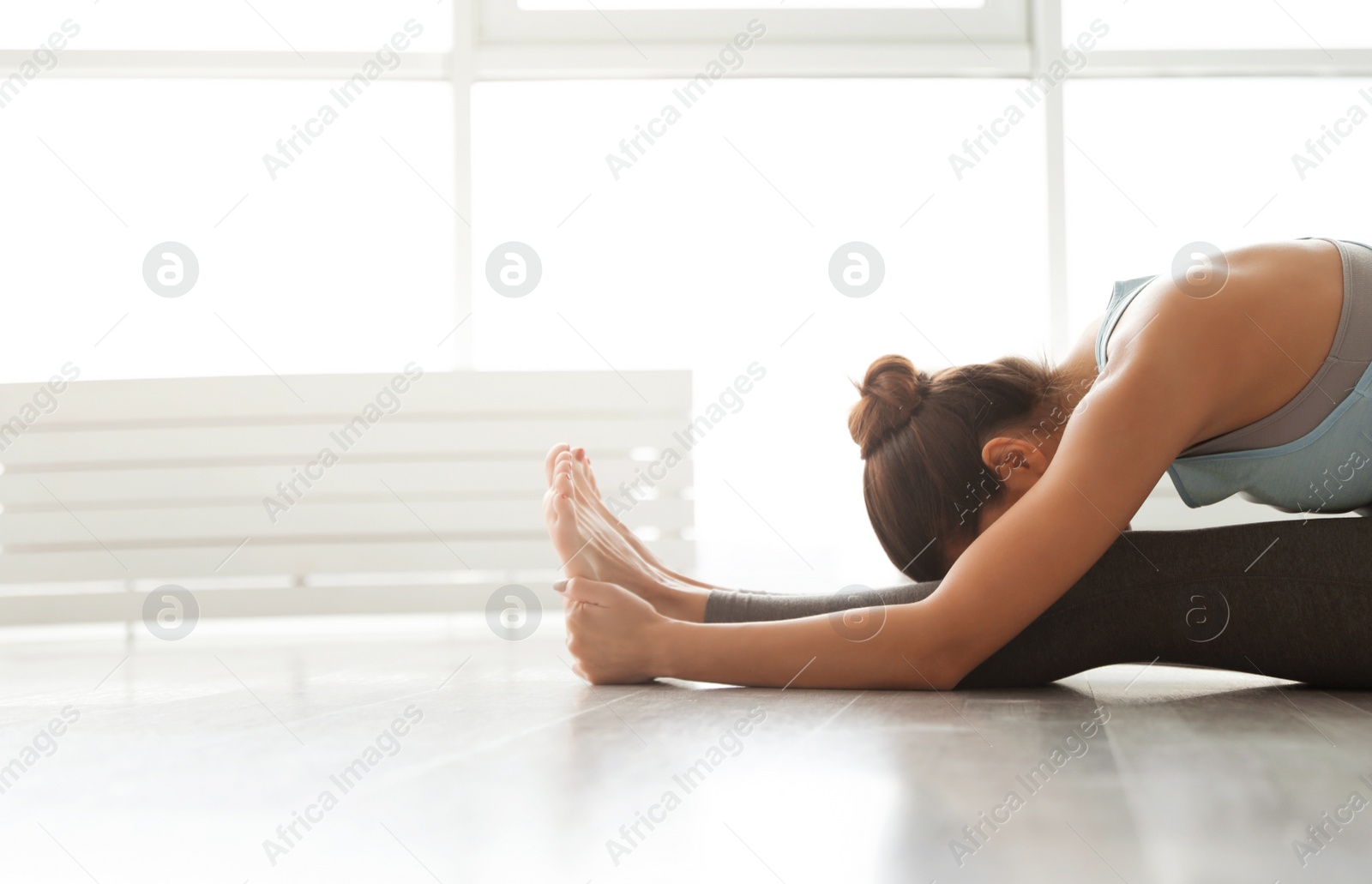 Photo of Young woman practicing seated forward bend asana in yoga studio. Pascimottanasana pose