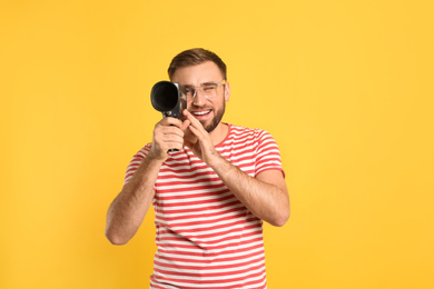 Young man using vintage video camera on yellow background