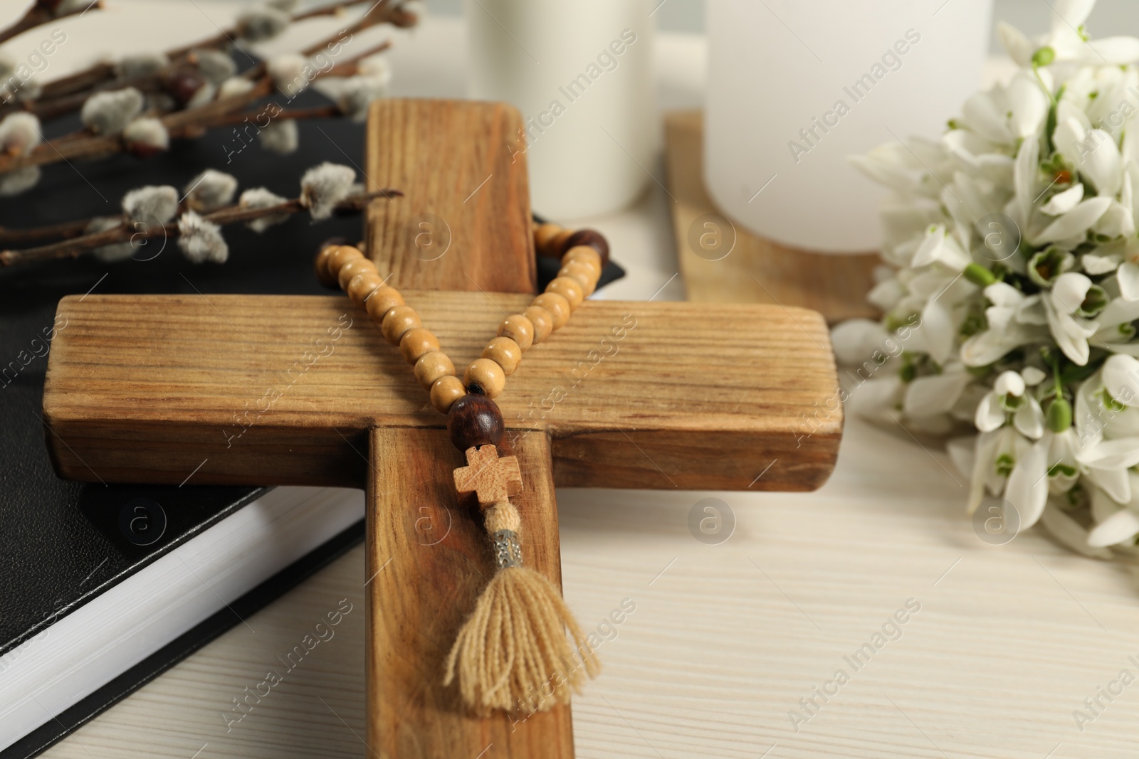 Photo of Wooden cross, rosary beads, Bible, willow branches and snowdrops on white table, closeup