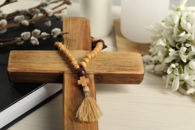 Photo of Wooden cross, rosary beads, Bible, willow branches and snowdrops on white table, closeup