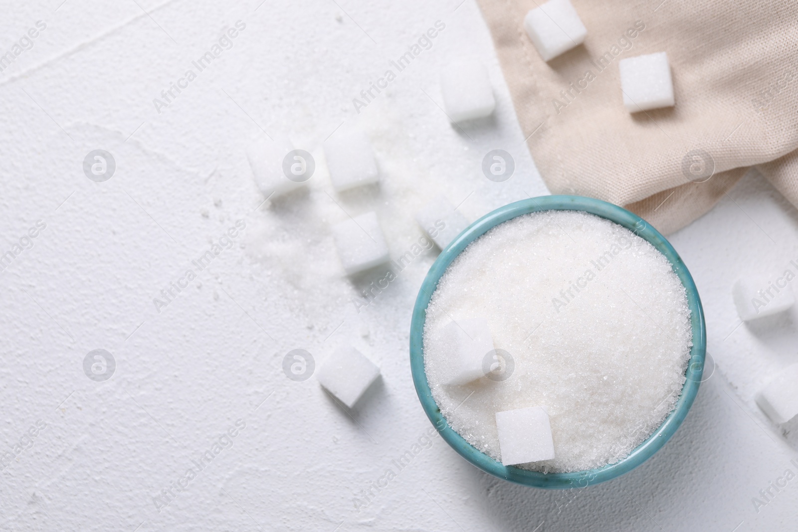 Photo of Different types of sugar in bowl on white table, flat lay. Space for text