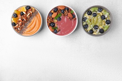 Bowls with different delicious fruit smoothies on white background, flat lay. Space for text