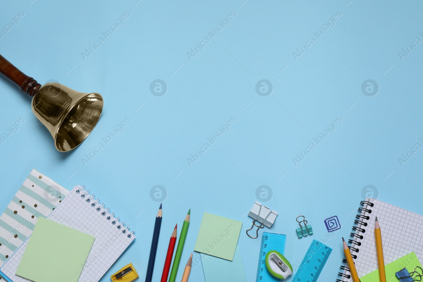 Photo of Different stationery and school bell on light blue background, flat lay. Space for text