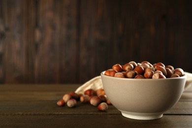 Ceramic bowl with hazelnuts on wooden table, space for text. Cooking utensil
