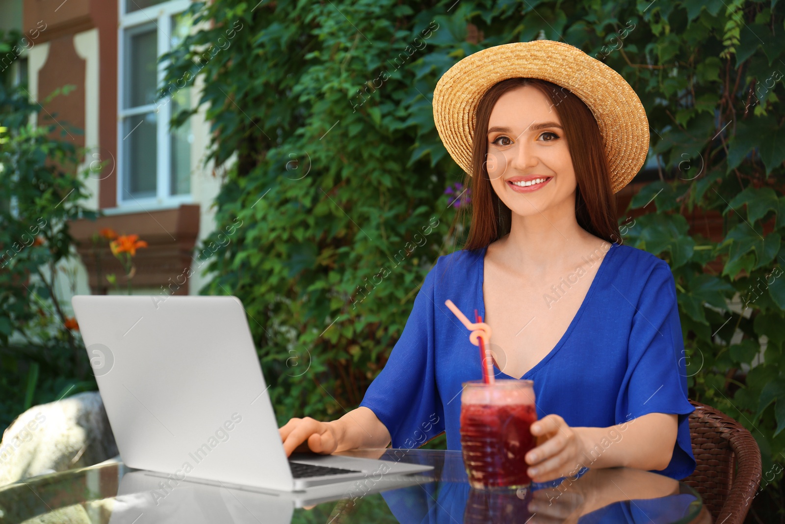 Photo of Beautiful young woman with glass of natural detox lemonade and laptop at table in outdoor cafe