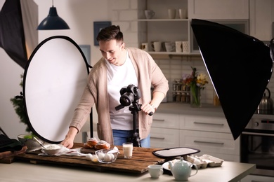 Young man with professional camera preparing food composition in photo studio