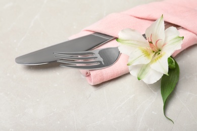 Photo of Folded napkin with fork, knife and flower on table, closeup