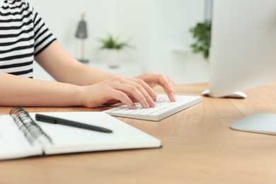 Home workplace. Woman typing on keyboard at wooden desk indoors, closeup