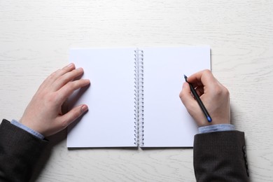 Photo of Man writing in notebook with pen at white wooden table, top view
