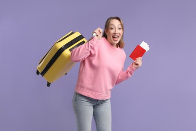 Photo of Emotional young woman with passport, ticket and suitcase on purple background