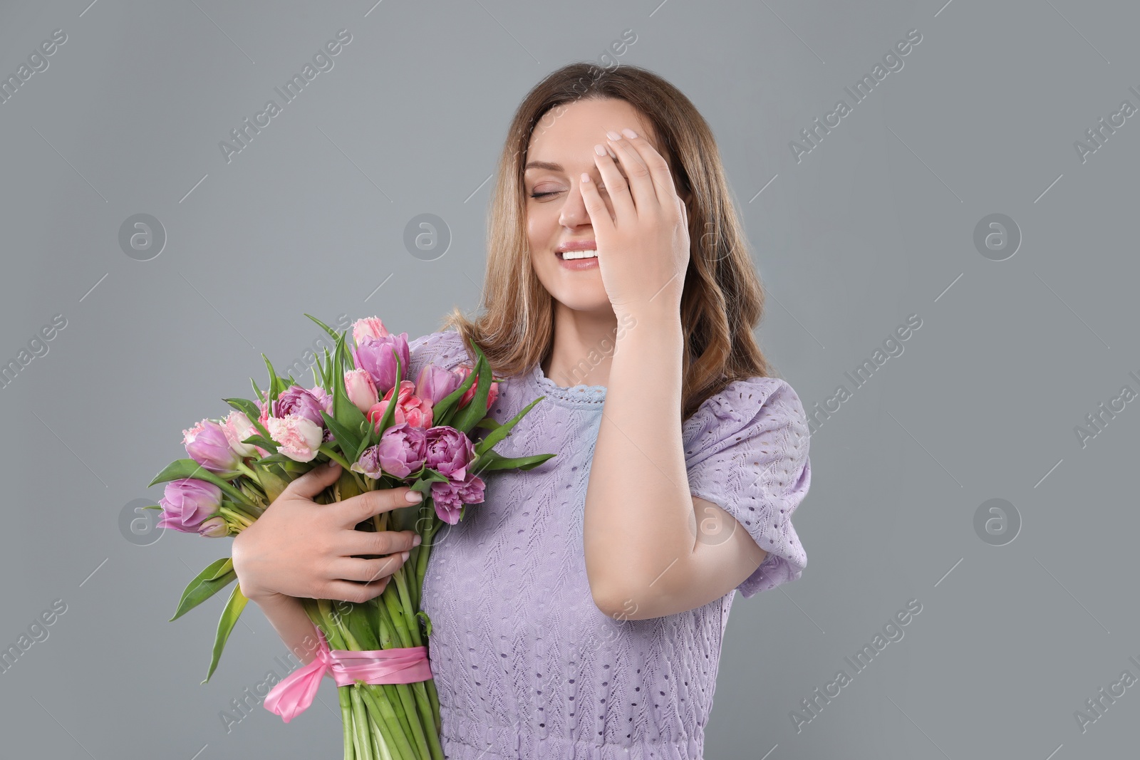 Photo of Happy young woman with bouquet of beautiful tulips on grey background