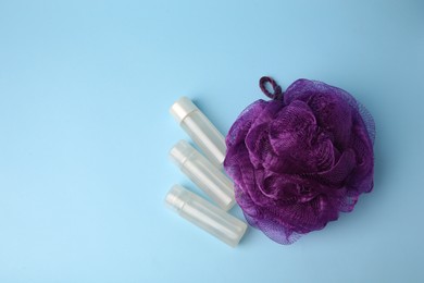 Photo of Purple shower puff and cosmetic products on light blue background, flat lay. Space for text