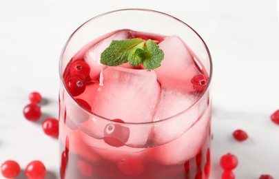 Tasty cranberry juice with ice cubes in glass and fresh berries on white wooden table, closeup