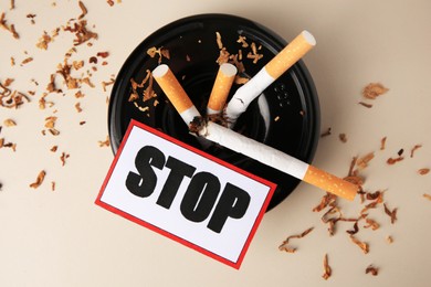 Photo of Card with word Stop, ashtray and cigarette stubs on beige background, flat lay. Quitting smoking concept