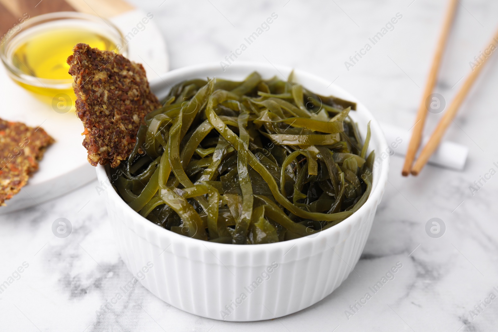 Photo of Tasty seaweed salad in bowl served on white marble table, closeup