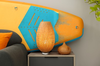 Photo of SUP board behind stylish sofa in room. Interior element