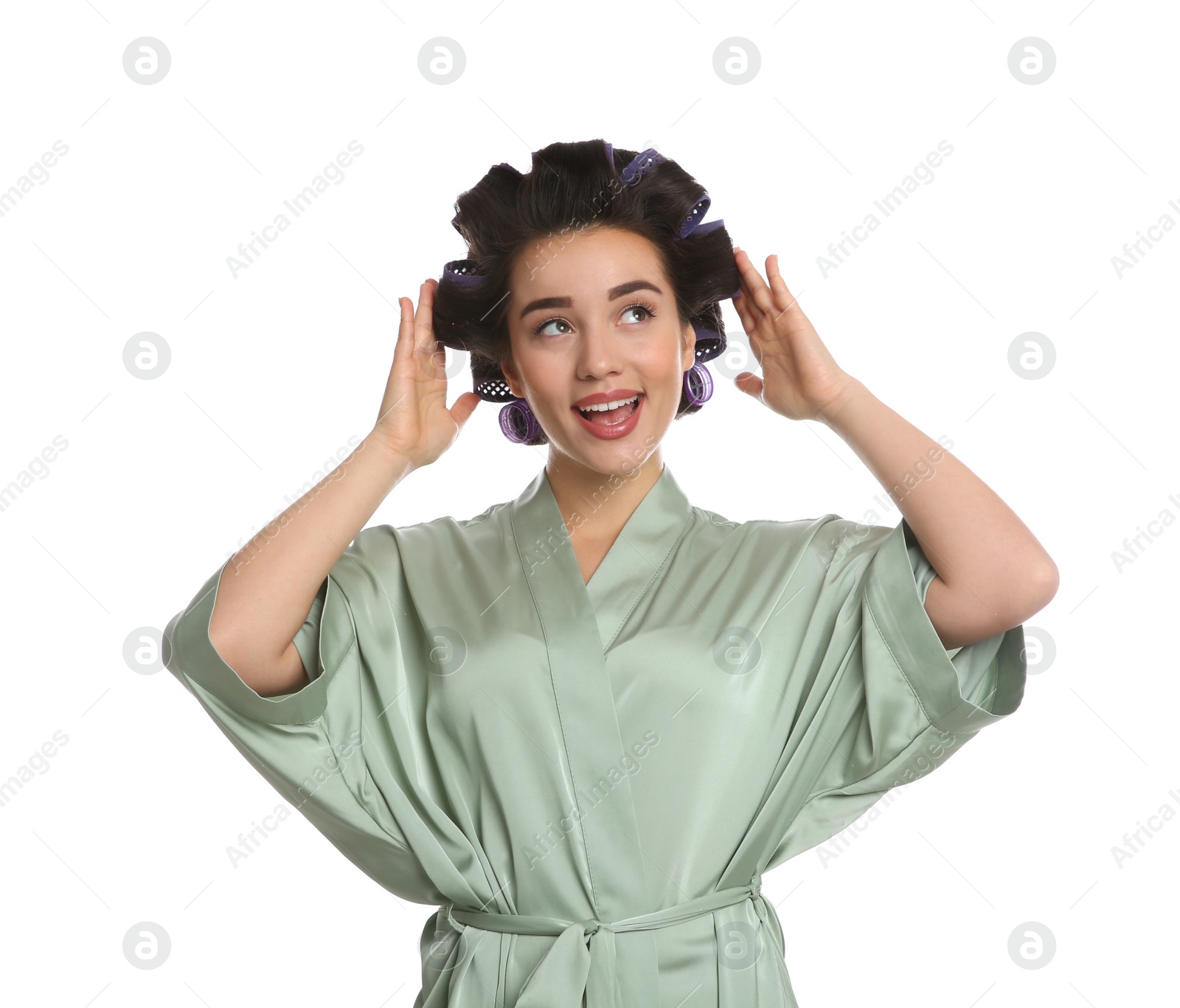 Photo of Happy young woman in silk bathrobe with hair curlers on white background