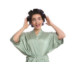 Happy young woman in silk bathrobe with hair curlers on white background