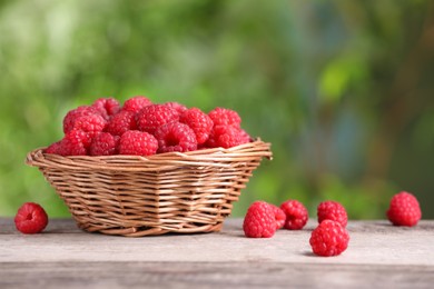 Photo of Wicker basket with tasty ripe raspberries on wooden table against blurred green background, closeup. Space for text
