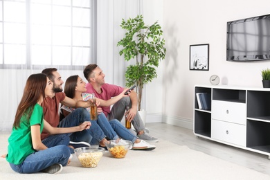 Photo of Young friends sitting on floor and watching TV at home