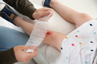 Father applying bandage on daughter's injured knee at home, closeup. First aid