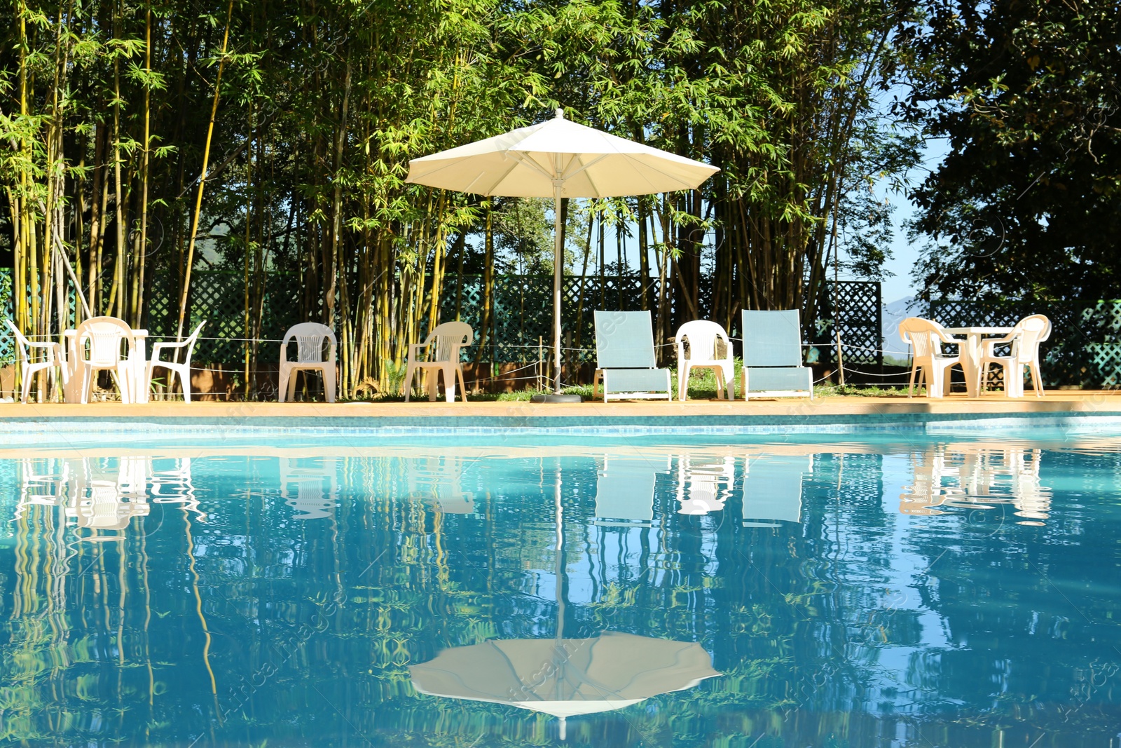 Photo of Pool with clean water, sunbeds and parasol outdoors