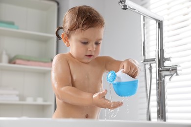Photo of Cute little girl playing with watering can in bathtub at home