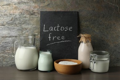 Photo of Dairy products and board with phrase Lactose Free on wooden table near grey wall