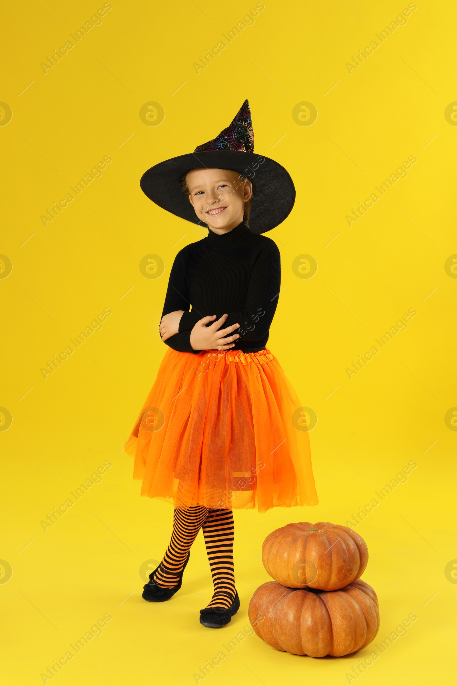 Photo of Cute little girl with pumpkins wearing Halloween costume on yellow background