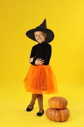 Photo of Cute little girl with pumpkins wearing Halloween costume on yellow background