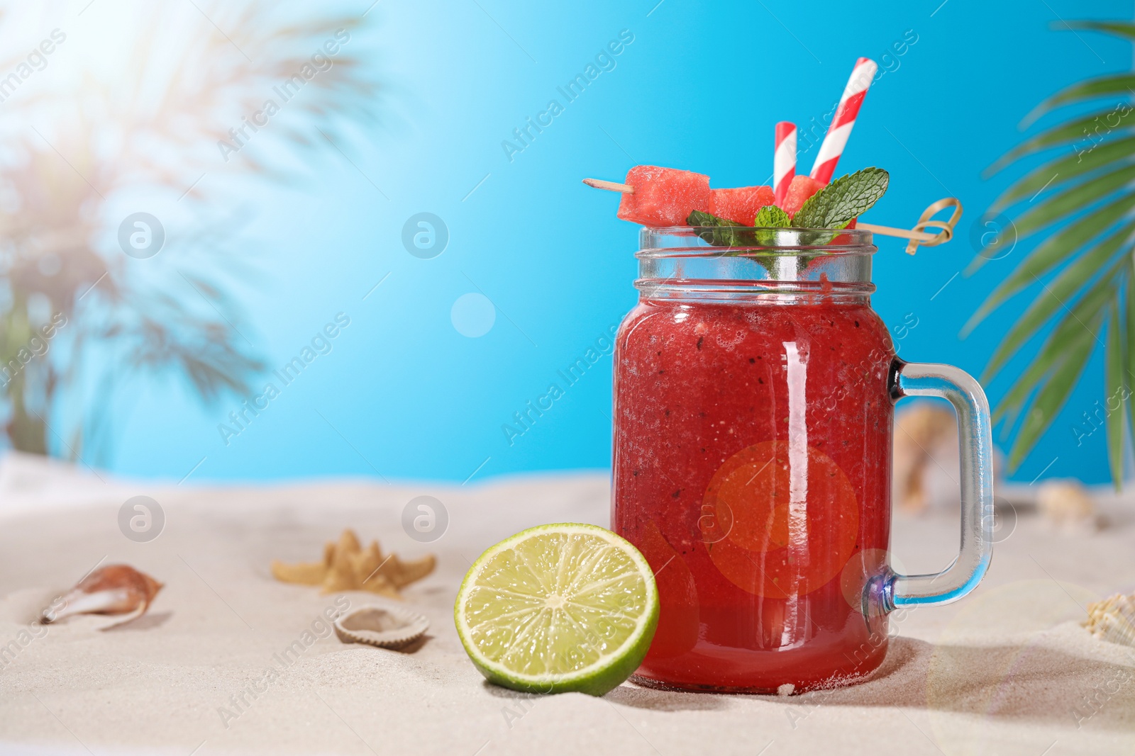 Photo of Tasty watermelon drink with lime in mason jar on sand, space for text