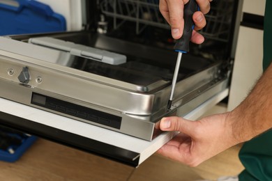 Serviceman repairing dishwasher door with screwdriver indoors, closeup