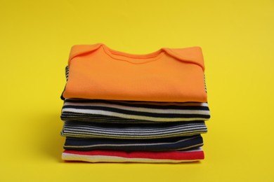 Stack of clean baby clothes on yellow background