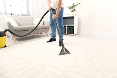 Photo of Man removing dirt from carpet with vacuum cleaner indoors, closeup