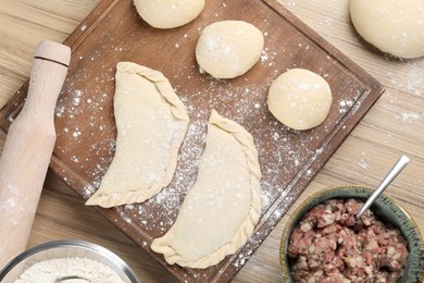 Photo of Raw chebureki with tasty filling and meat in bowl on wooden table, flat lay