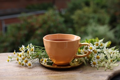 Photo of Cup of delicious chamomile tea and fresh flowers outdoors