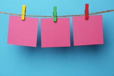 Photo of Wooden clothespins with blank notepapers on twine against light blue background. Space for text