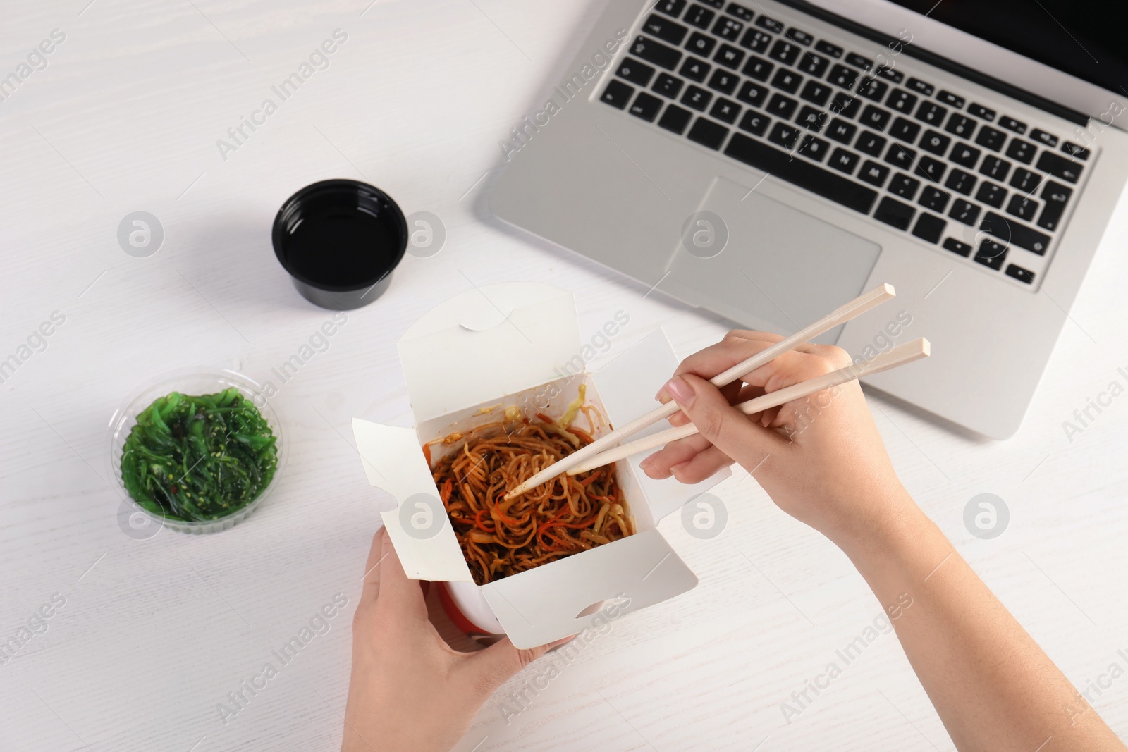 Photo of Woman eating tasty Chinese noodles at workplace, closeup. Food delivery