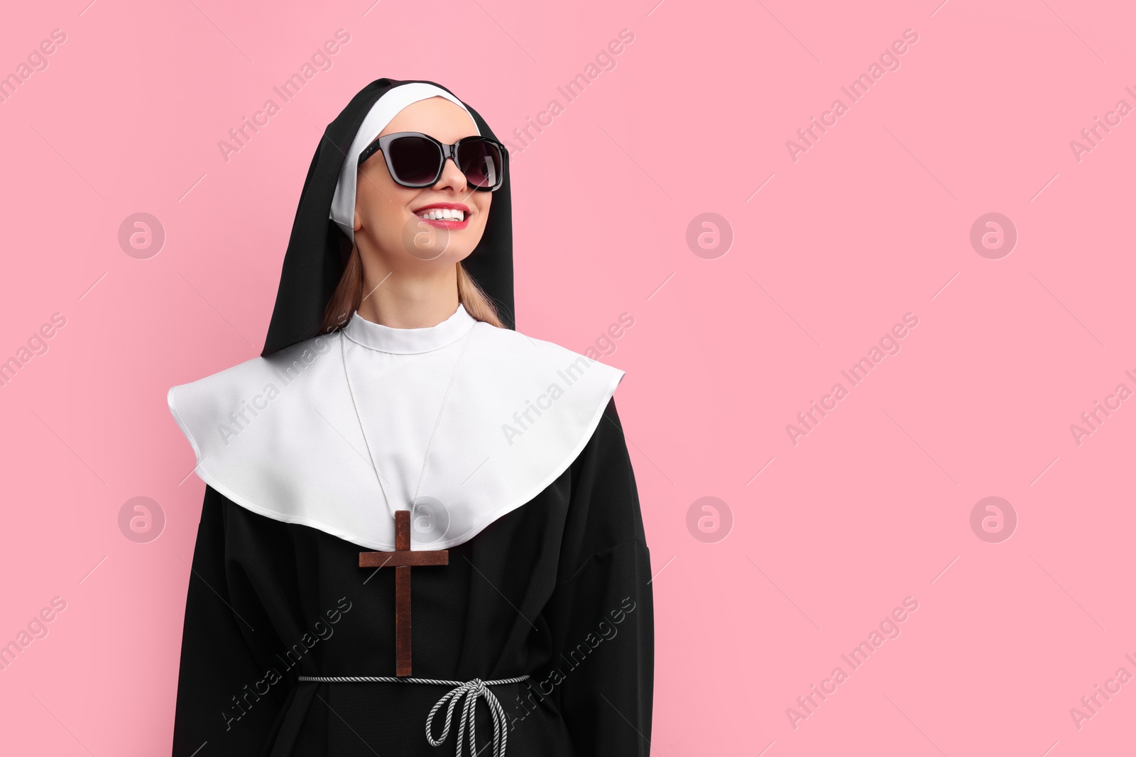 Photo of Woman in nun habit and sunglasses against pink background. Space for text