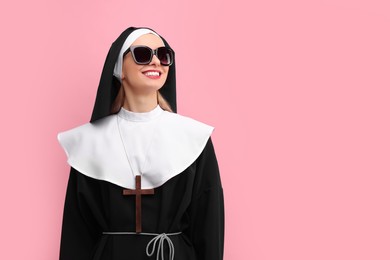 Woman in nun habit and sunglasses against pink background. Space for text