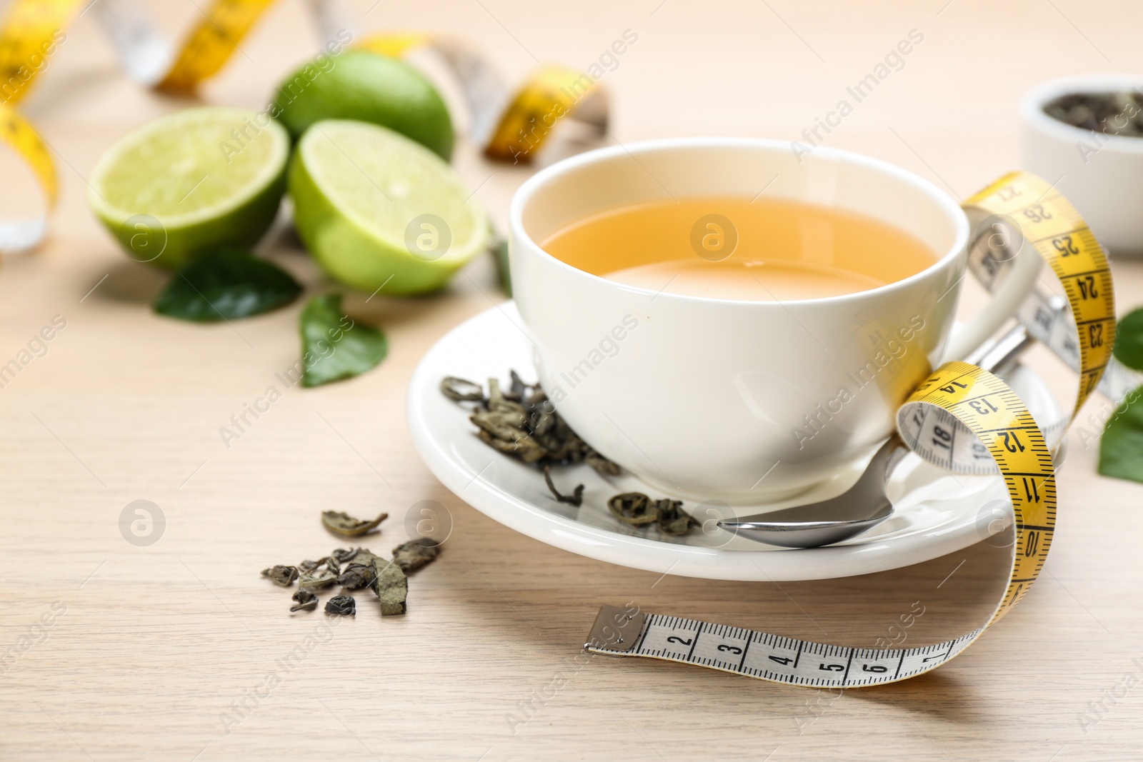 Photo of Cup of diet herbal tea, measuring tape and dried leaves on wooden table