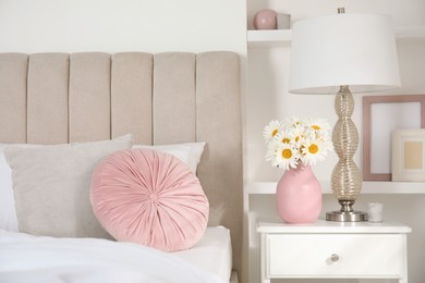 Photo of Bouquet of beautiful daisy flowers and lamp on nightstand in bedroom