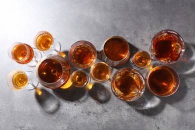 Different delicious liqueurs in glasses on grey table, flat lay