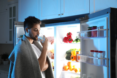 Young man drinking milk near open refrigerator at night