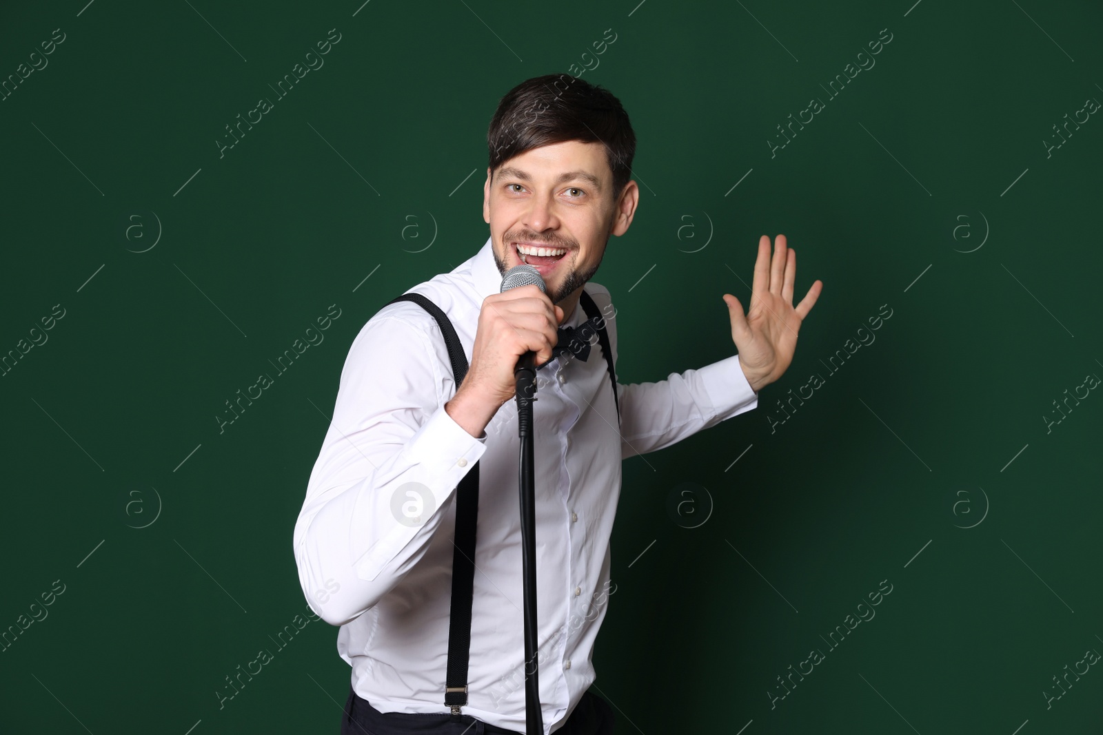 Photo of Handsome man in formal clothes singing with microphone on color background